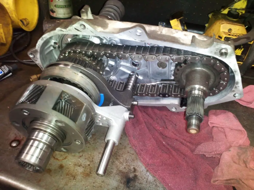 Close-up internal view of an opened transfer case, clearly showing the drive chain, sprockets, and various gears within the housing.