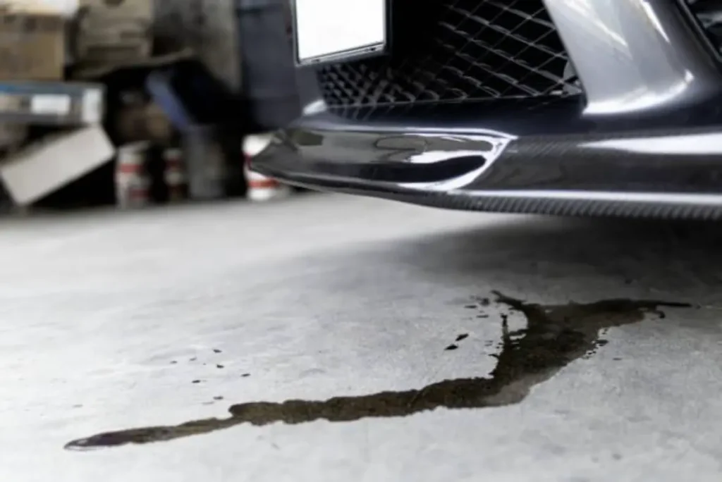Dark fluid puddle on concrete beneath the front bumper of a vehicle, indicating a leak, potentially from the transfer case.