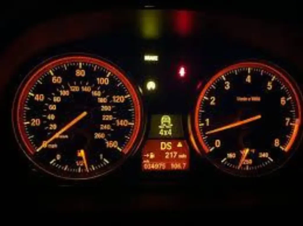 Vehicle dashboard illuminated at night, showing the speedometer and tachometer, with a prominent '4x4' warning light glowing orange in the center display.
